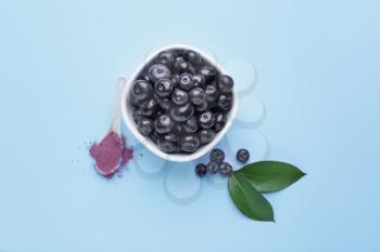 Bowl with fresh acai berries and spoon with powder on color background�