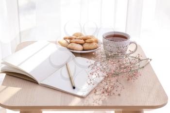 Cup of hot tea with notebook and cookies on table�