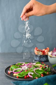 Woman sprinkling salt onto tasty salad on plate�