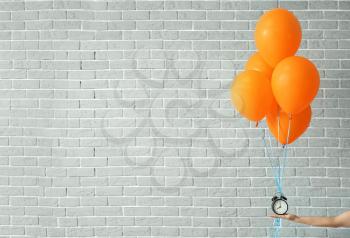 Female hand with air balloons and alarm clock on grey brick background�