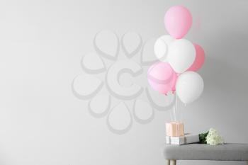 Air balloons with gift boxes and flowers on bench against light background�