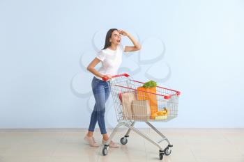 Young woman with shopping cart near color wall�