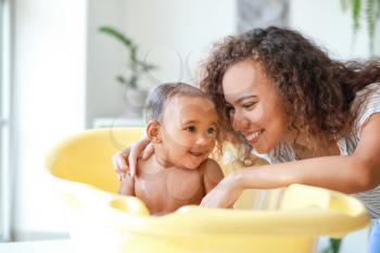 Young African-American mother washing her baby at home�