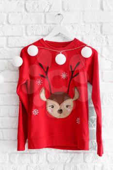 Hanger with Christmas sweater and garland on white brick wall�
