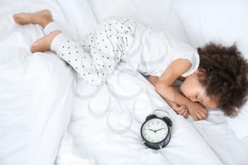 Little African-American girl with alarm clock sleeping in bed�