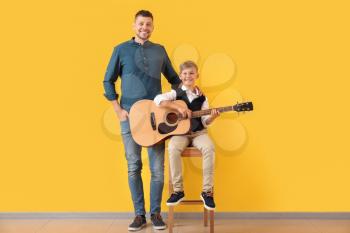 Handsome man and his little son with guitar near color wall�