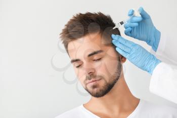 Man with hair loss problem receiving injection on grey background�