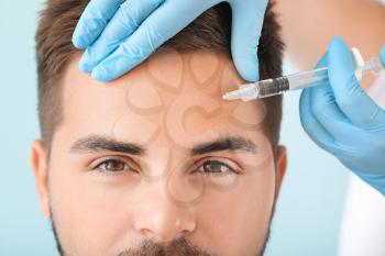 Handsome man receiving filler injection on color background, closeup�