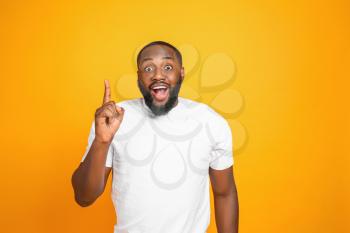 Surprised African-American man with raised index finger on color background�