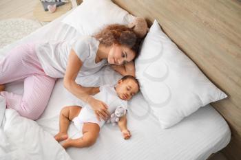 Young African-American woman and her sleeping baby on bed�