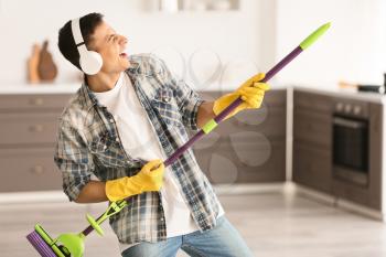 Young man listening to music and singing while cleaning kitchen�