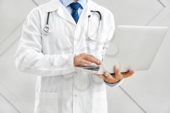 Male doctor with laptop on light background�
