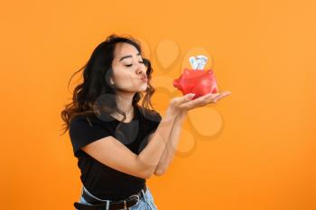 Happy Asian woman with piggy bank on color background�