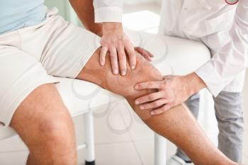 Doctor examining mature man with joint pain in clinic�