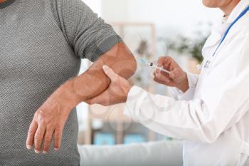 Doctor giving mature man with joint pain injection at home, closeup�