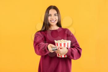 Young woman with popcorn and remote control on color background�