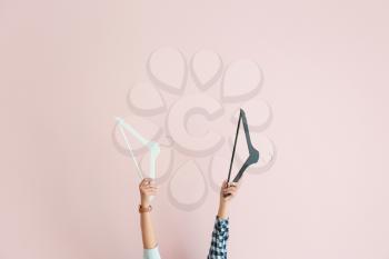 Female hands with clothes hangers on color background�