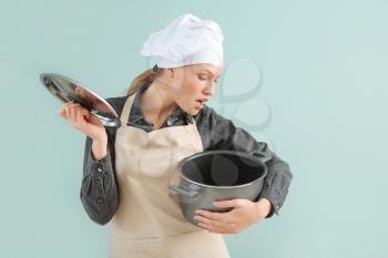 Beautiful female chef with saucepan on color background�