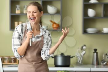 Beautiful young woman singing while cooking in kitchen�