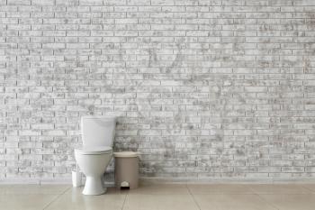 Toilet bowl near light brick wall�