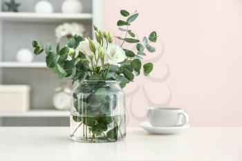 Vase with beautiful flowers and cup of tea on table in room�