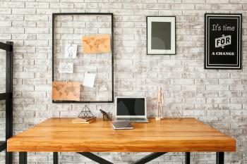 Comfortable workplace with mood board and laptop near brick wall�
