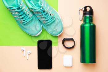 Sports water bottle, shoes, mobile phone and gadgets on color background�
