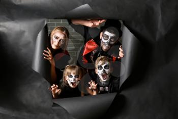Family in Halloween costumes looking out of hole in torn paper�