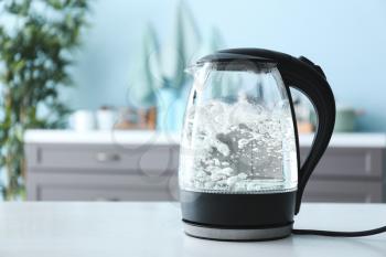 Transparent electric kettle with boiling water on table in kitchen�