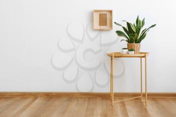 Table with green houseplants near white wall in room�