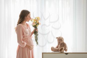 Beautiful pregnant woman with flowers near window�