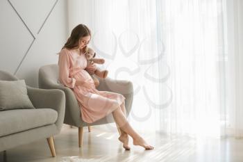 Beautiful pregnant woman with toy sitting in armchair at home�