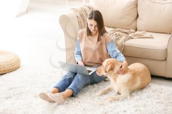Beautiful young woman with cute dog using laptop at home�