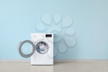 Modern washing machine with laundry near color wall�
