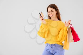 Beautiful young woman with shopping bags and credit card on light background�