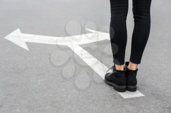 Young woman standing on road with arrows marking. Concept of choice�