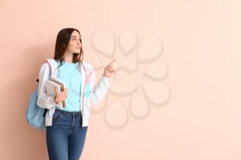 Portrait of teenage schoolgirl pointing at something on color background�