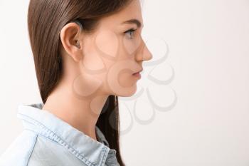 Young woman with hearing aid on light background�
