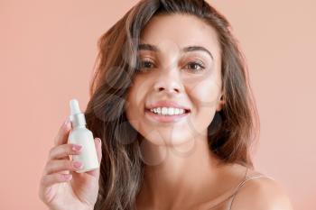 Beautiful young woman with bottle of serum on color background�