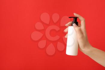 Female hand with cosmetic product in bottle on color background�