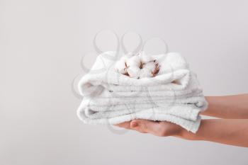 Female hands with beautiful cotton flowers and soft towels on grey background�
