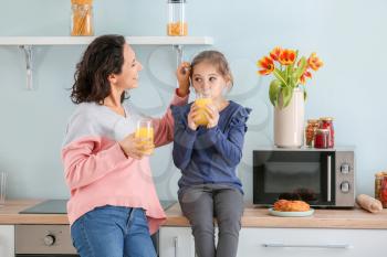 Little girl with her mother drinking juice in kitchen�
