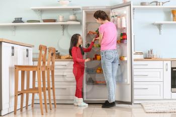 Little girl and her mother choosing food from fridge in kitchen�