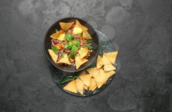 Bowl with tasty chili con carne and nachos on dark background�