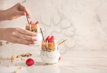 Female hands with glass of tasty granola and yogurt on white background�