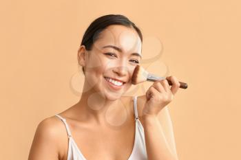Portrait of young Asian woman with makeup brush on color background�