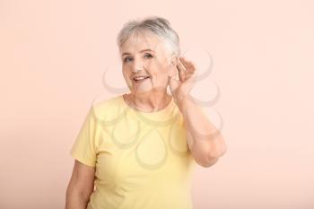 Senior woman with hearing aid on color background�