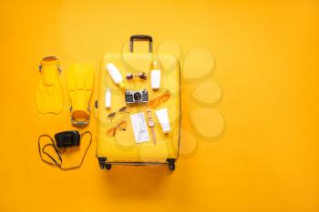 Suitcase with travel accessories on color background�