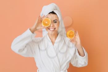 Beautiful young woman in bathrobe and with oranges on color background�