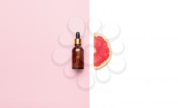Bottle of essential oil and grapefruit slice on color background�